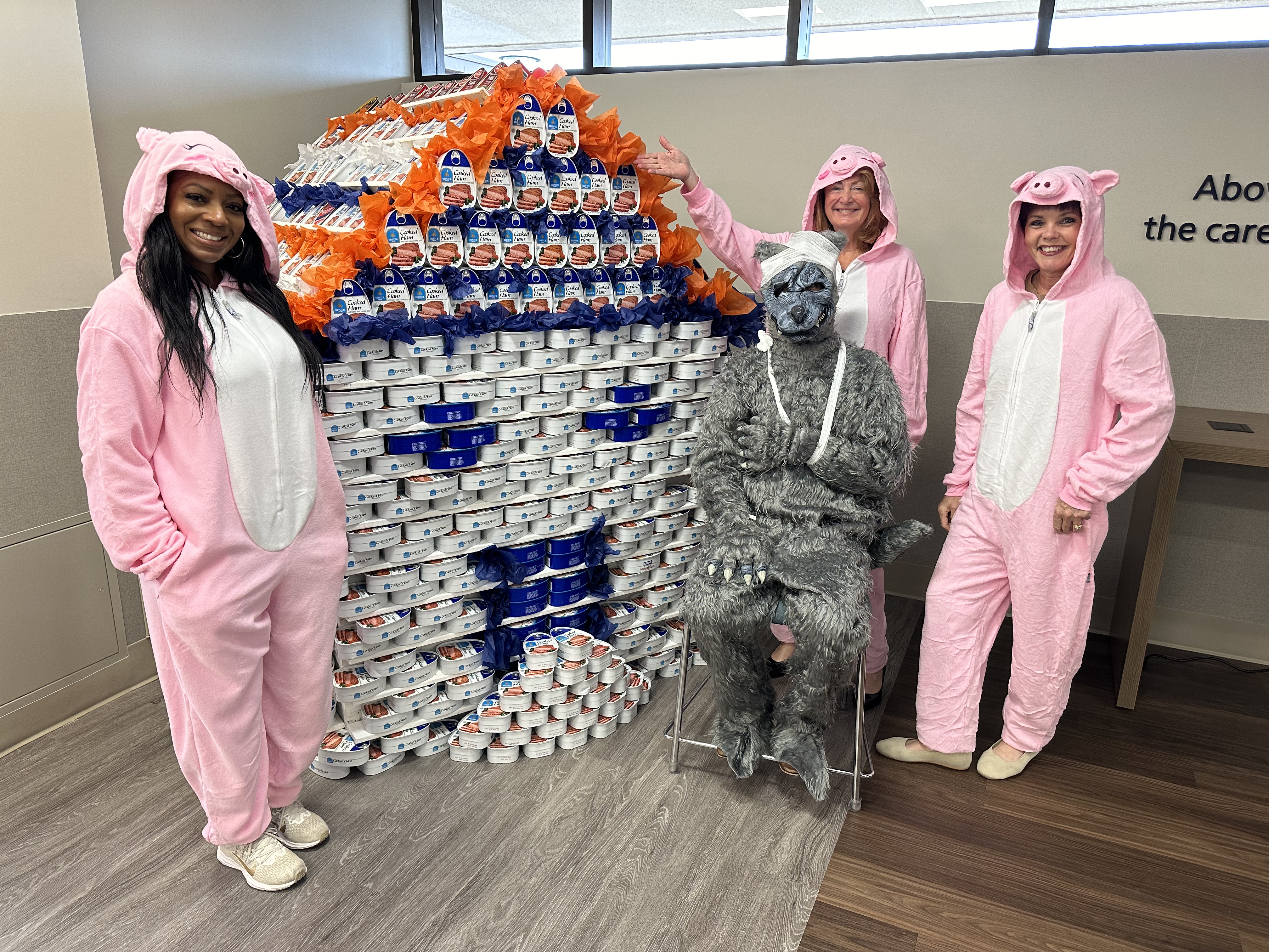 Hospital staff dressed as the Big Bad Wolf and Three Little Pigs pose in front of their house shaped sculpture made of canned food.