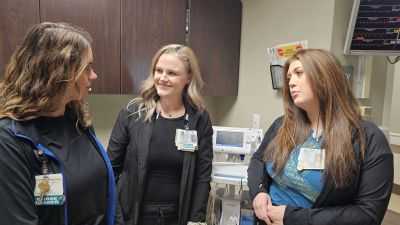 Three nurses smile while talking with each other in the hospital.