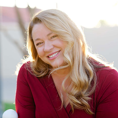 Alison Henriksen smiling with her head tilted to one side, wearing a red, long-sleeve shirt.