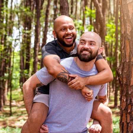 Two men in a forest, one is giving the other a piggy back ride.