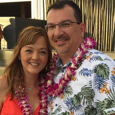 Frank Noe and his wife wear Hawaiian leis around their necks, smiling.