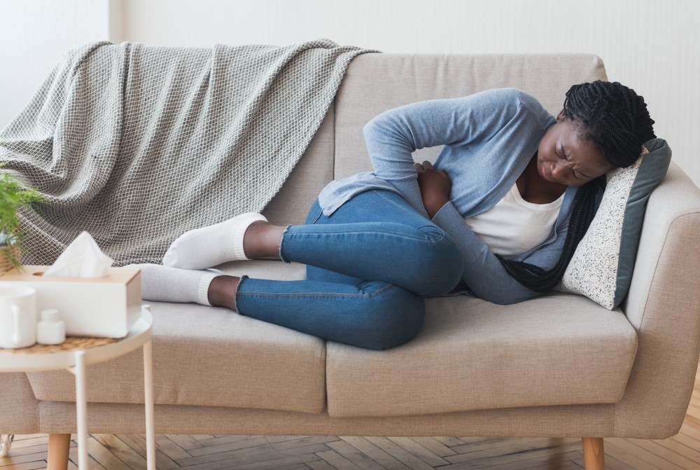 A woman with stomach pain lies on a couch with her hand on her abdomen.