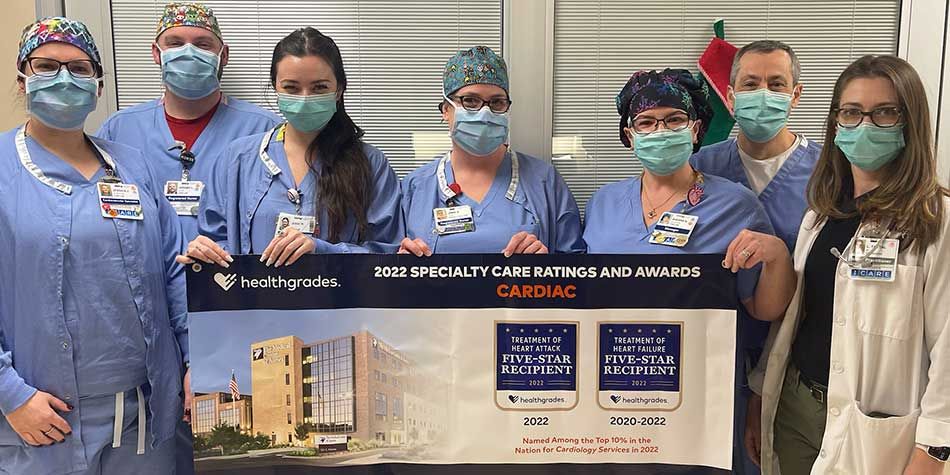The Medical Center of Aurora Cardiac and Vascular Center team pose in scrubs while holding an awards banner by Healthgrades that reads, "2022 Specialty Care Ratings and Awards: Cardiac"