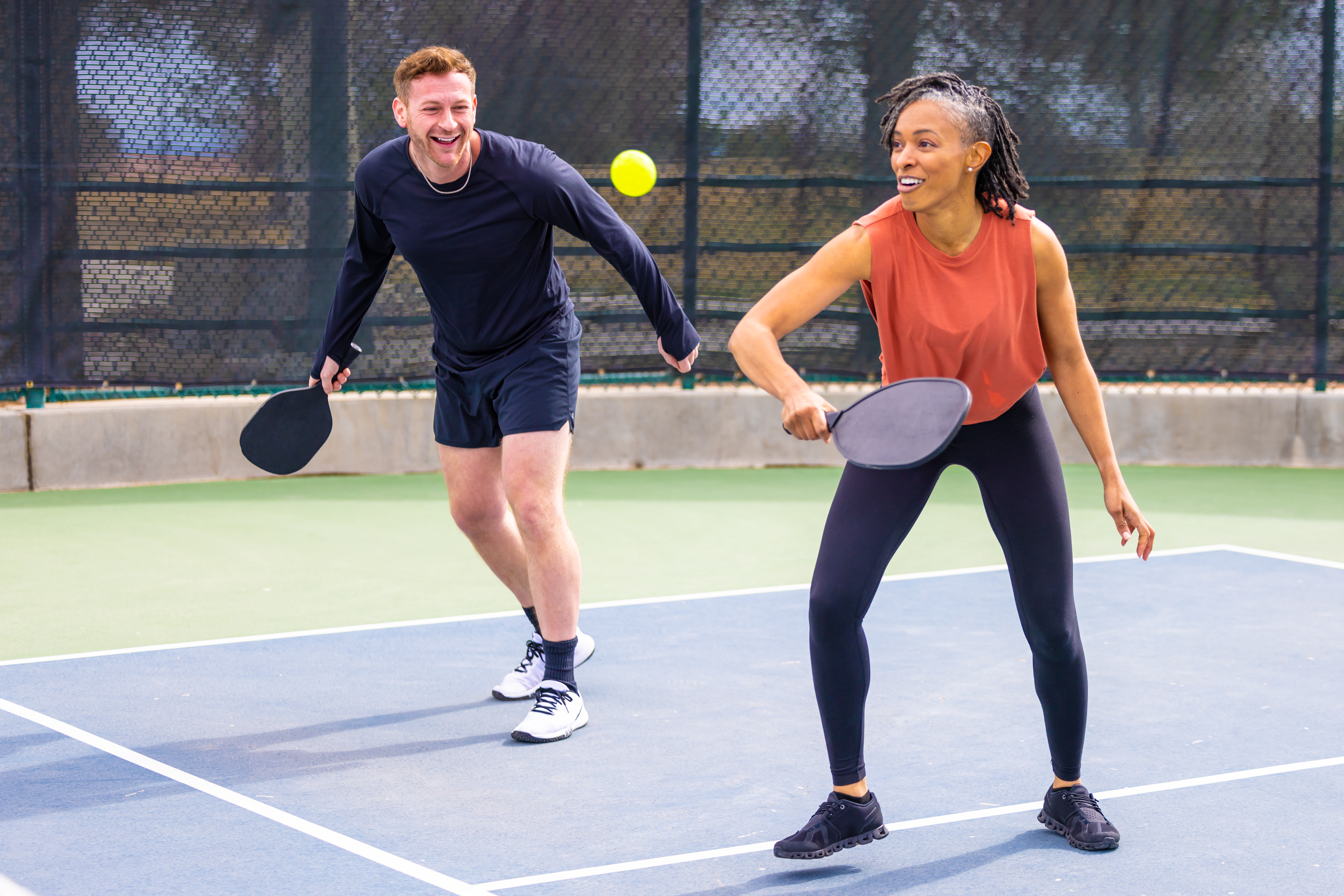 Black woman playing pickleball with white male partner on an outdoor court.