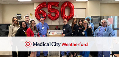 Hospital staff smile while standing next to a cake with the Medical City logo on it to celebrate the 650th robotic surgery procedure. There is text on the picture that reads, "Medical City Weatherford."