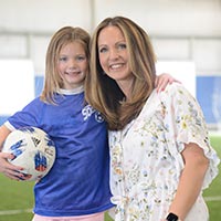 Amanda and her daughter, Emma, smile while embracing after one of Emma's soccer practices.