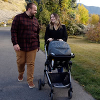 Kaeden and Emily smile while walking their daughter, Remi, in a stroller.