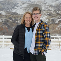 Ben and Jill Winters stand together with a wintery mountain and white farm fence in the background.