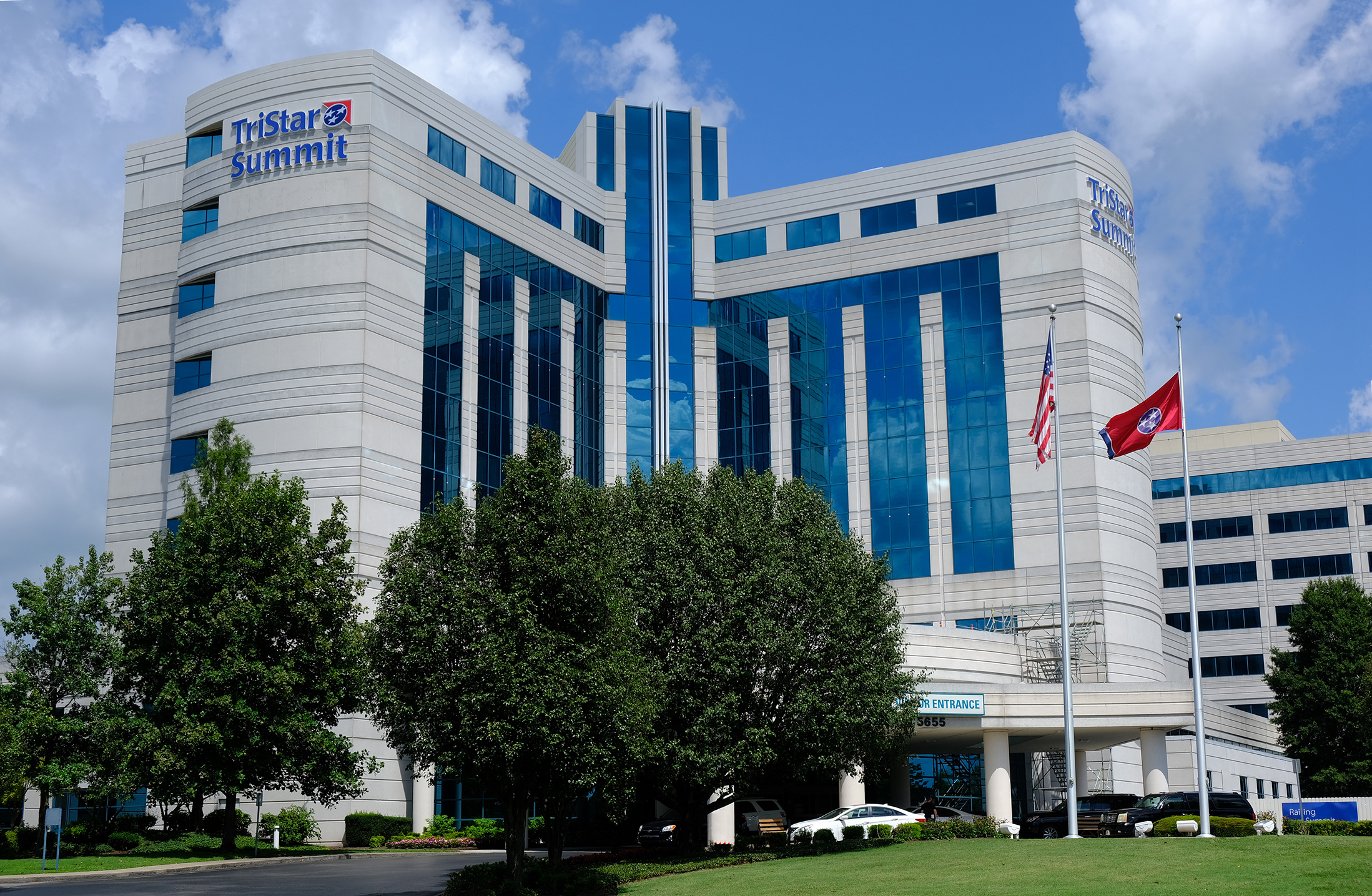 Tristar Summit Medical Center as seen from the street. An American and Tennessee State flags on flagpoles, stout trees, and a roofed parkway at the entrance.
