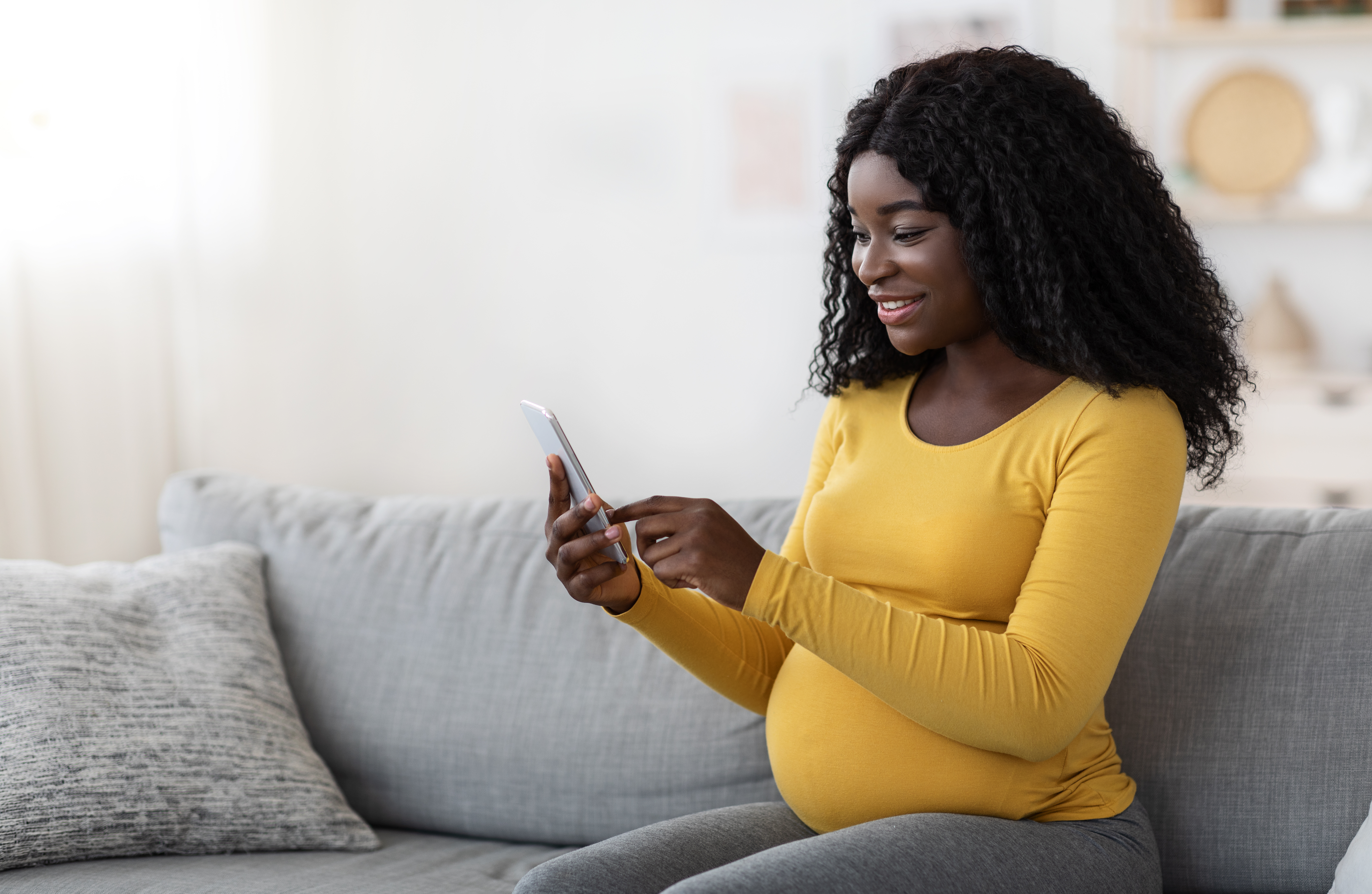 Expectant mom smiles while looking at her smartphone.