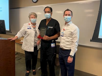 Dr. Mathew Ninan stands between two Trinity hospital staff members in a classroom setting. 