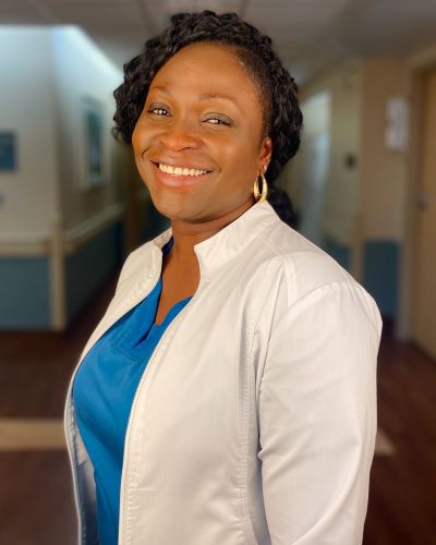 Joyce Arthur smiles while wearing blue hospital scrubs and a white lab coat.