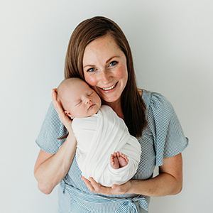 Crystalee Beck smiling while holding her swaddled newborn baby boy.