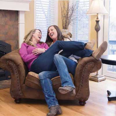 Jody and her daughter, Lauren, laugh and smile together while sitting in a lounge chair in their living room.