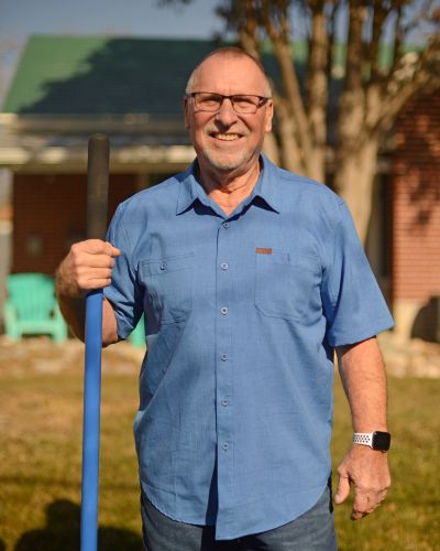 Bill Zierse standing outside holding a rake.
