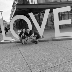 Stroke survivor, Will Shen, with his wife and child, standing next to a public art sculpture outside of a city building that spells out Love.