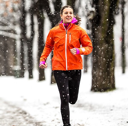 A woman jogs during winter, while it is snowing.