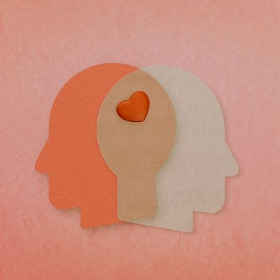 On a textured light pink background, illustrated heads in orange and white intersect at the head with a red heart displayed where the heads intersect. 