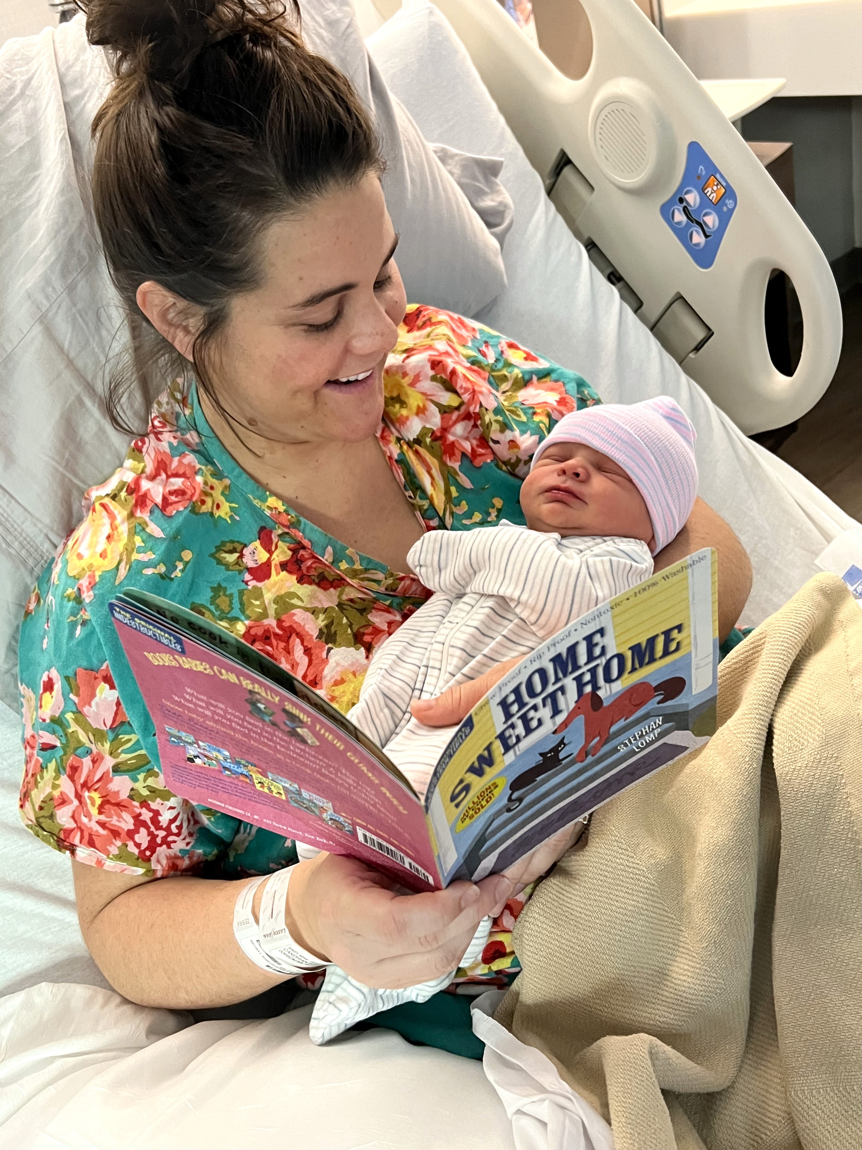 A woman in bed reading a book to an infant she is holding.