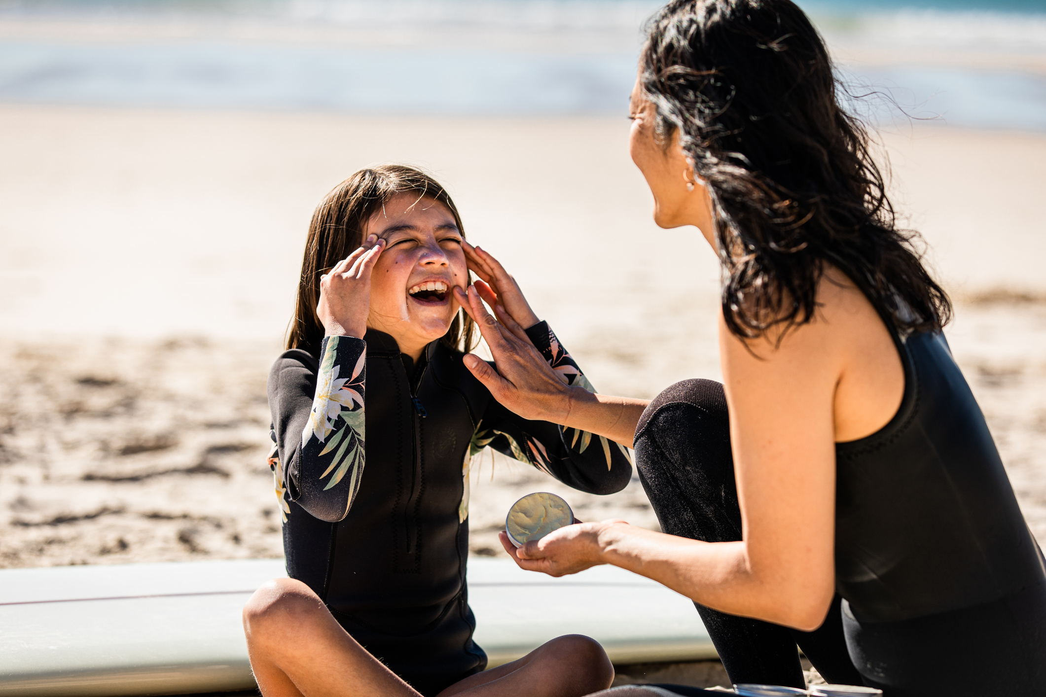 Mother applies sun tan lotion to daughter's face at the beach.