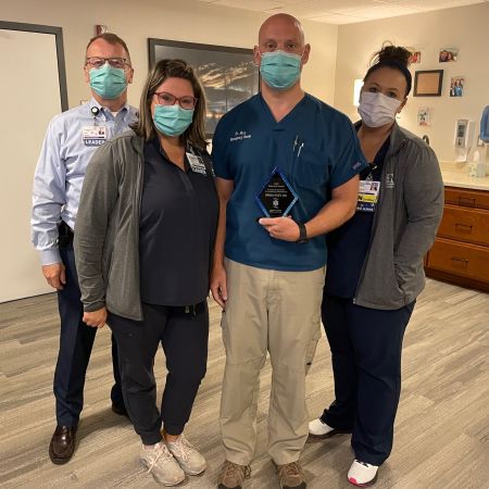 Brian Ekey holding the Dr. Cheryl B. Haas Award for Outstanding EMS Physician while posing with Devin Tobin, chief operations officer, and two other female team members.