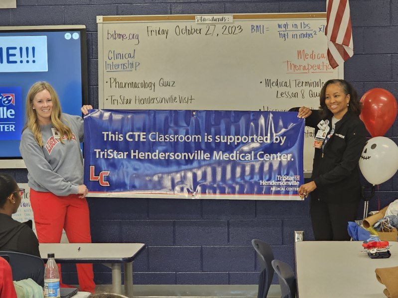 Volunteers pose with CTE classroom banner.