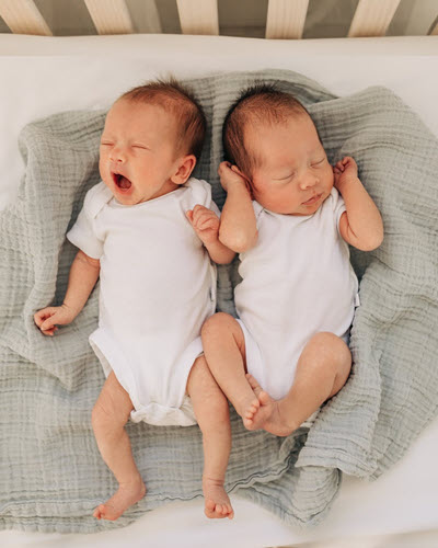 Jenn Glazier's twins, Rosie and Nora, cuddle and yawn while lying together on a grey blanket.