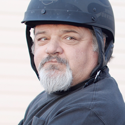 Martin looks over his should while wearing a black motorcycle helmet and t-shirt.