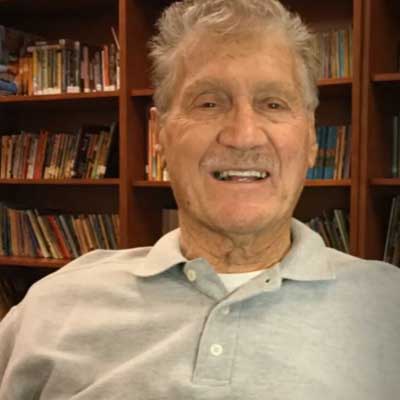 Eugene Potestio smiles while wearing a grey polo shirt and sitting in a library.