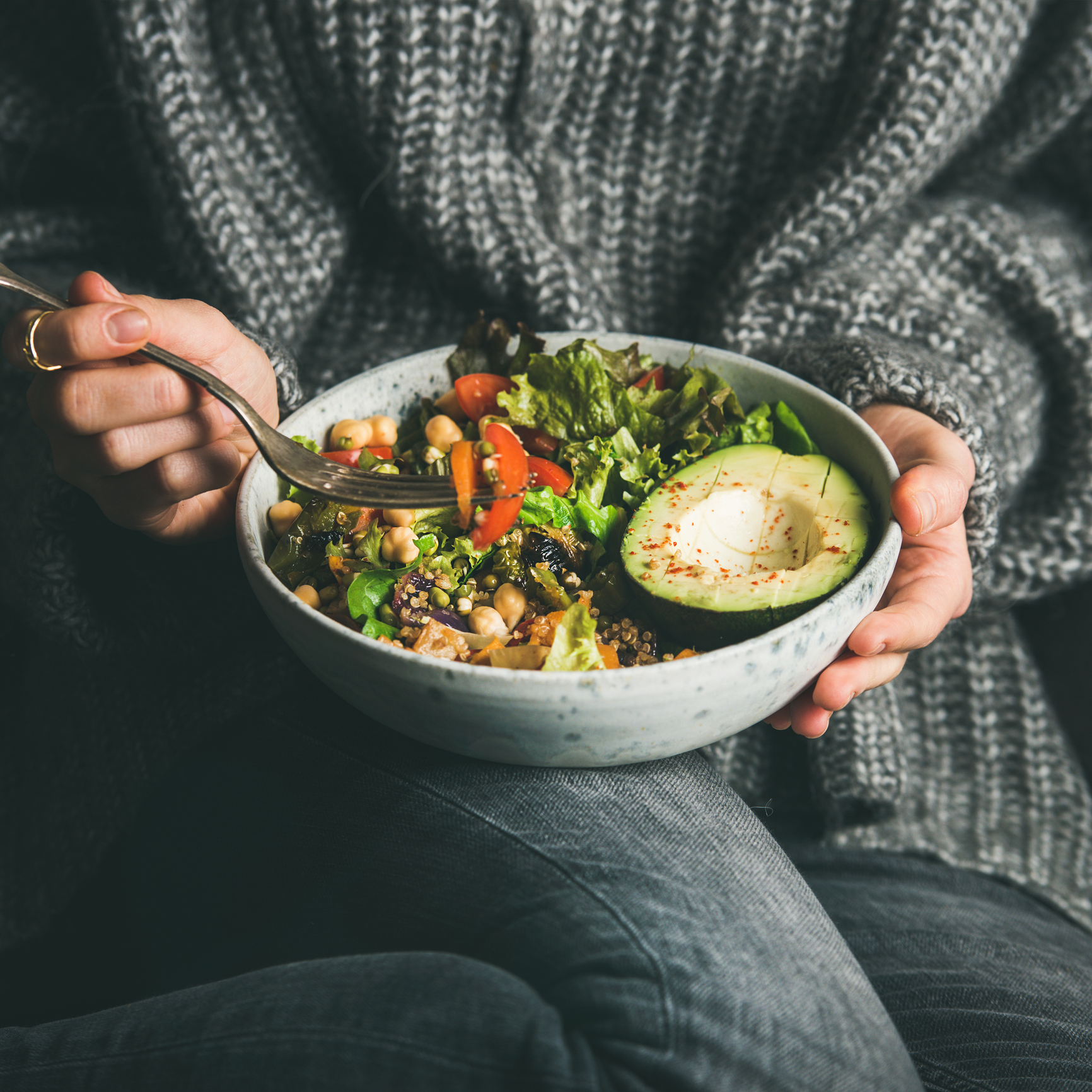 Woman holding a bowl of salad with sliced avocado on one side.