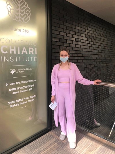 Brain surgery survivor Hannah Jane standing beside the Colorado Chiari Institute sign.