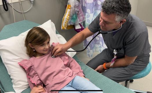 A girl smiles while a doctor uses a stethoscope to listen for her heartbeat.