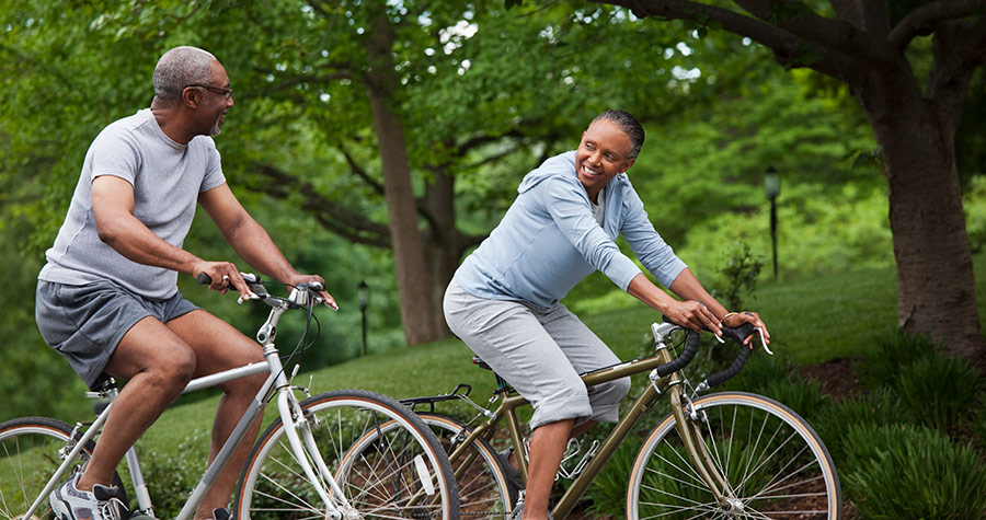 A couple smiles while riding bicycles together in a park.