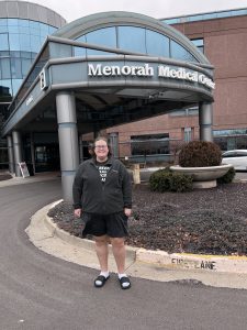 Ali Liggett smiles while standing next to the Menorah Medical Center front entrance.