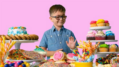 Young boy surrounded by doughnuts, cake, cupcakes, and cookies.