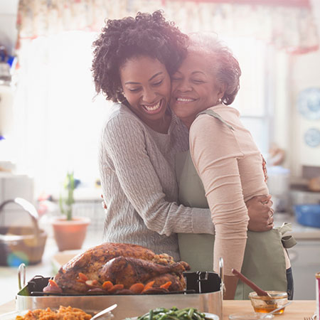 A mother and daughter hug and smile while standing in their kitchen during Thanksgiving.