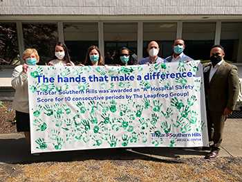 A group of hospital staff are standing outside holding a large banner with green handprints covering the surface. The banner reads, 'The hands that make a difference. TriStar Southern Hills was awarded an 'A' Hospital Safety Score for 10 consecutive periods by The Leapfrog Group!'