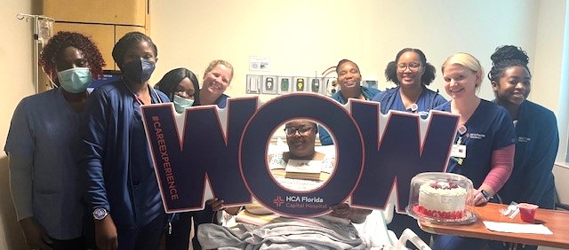 Cynthia Parks and hospital staff holding a WOW sign with her face showing through the "O", while in hospital bed