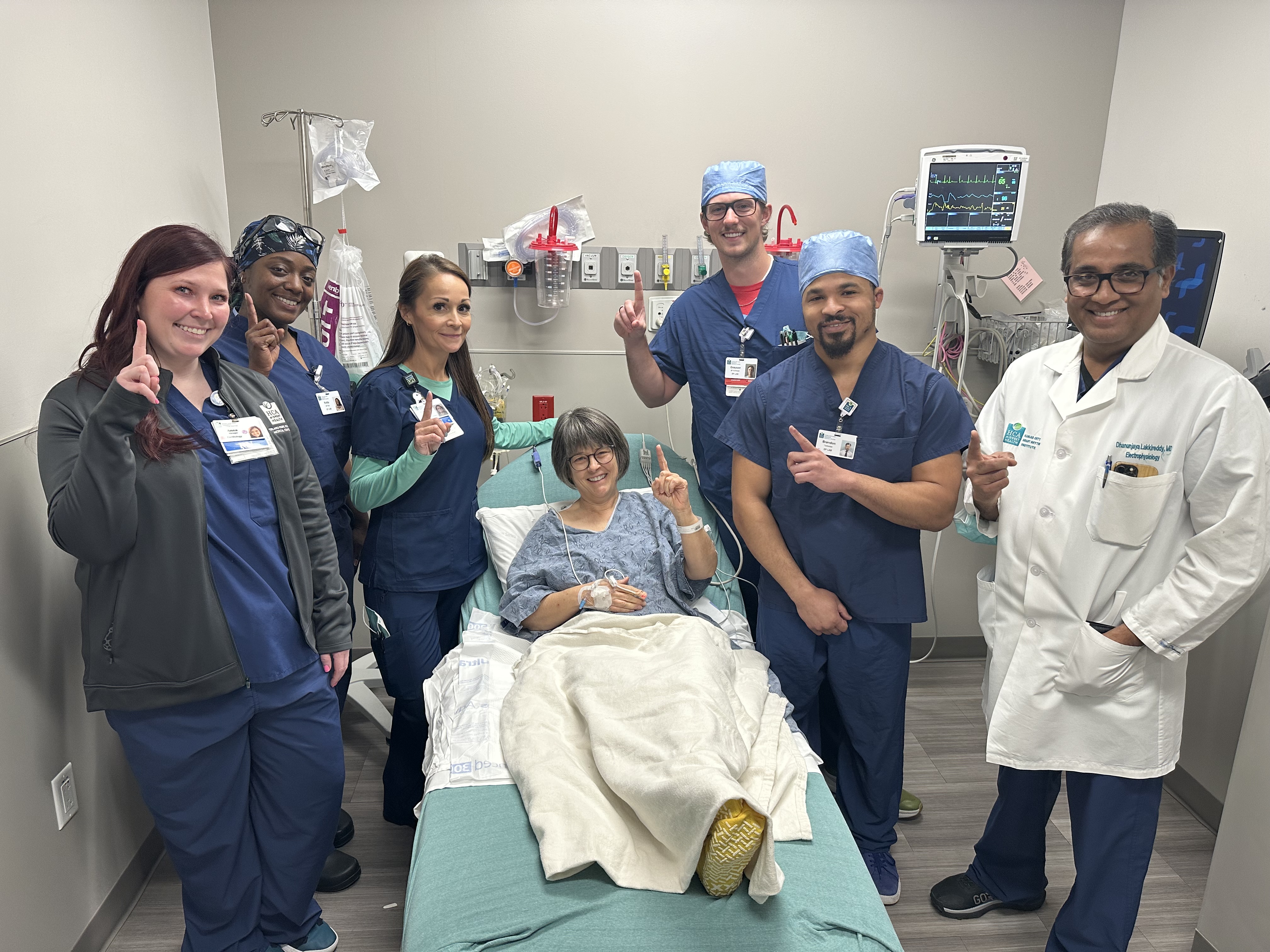 Dr. Lakkireddy and nurses stand beside patient Kristine Benson's bed, each holding up their index fingers in recognition of this first-time procedure.
