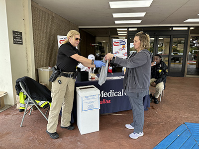 A hospital staff member hands a bag of old medication to a police officer.