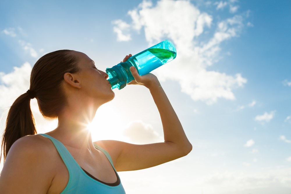 A woman drinks from a bottle of water outside in the sun
