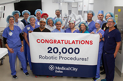 Surgery staff from Medical City Dallas smile while holding a banner with the text, "Congratulations 20,000 Robotic Procedures! Medical City Dallas."
