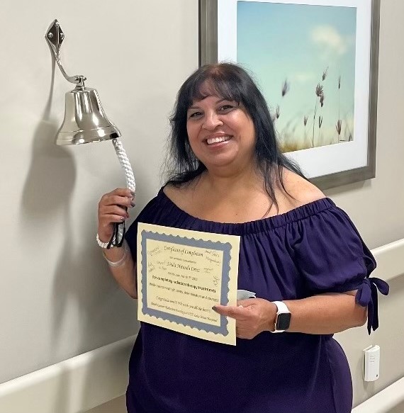 Neida Miranda holding a certificate and ringing a bell