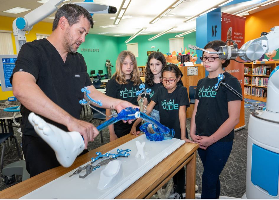 Dr. John Thomas shows off surgical robot to students in brightly-colored school room