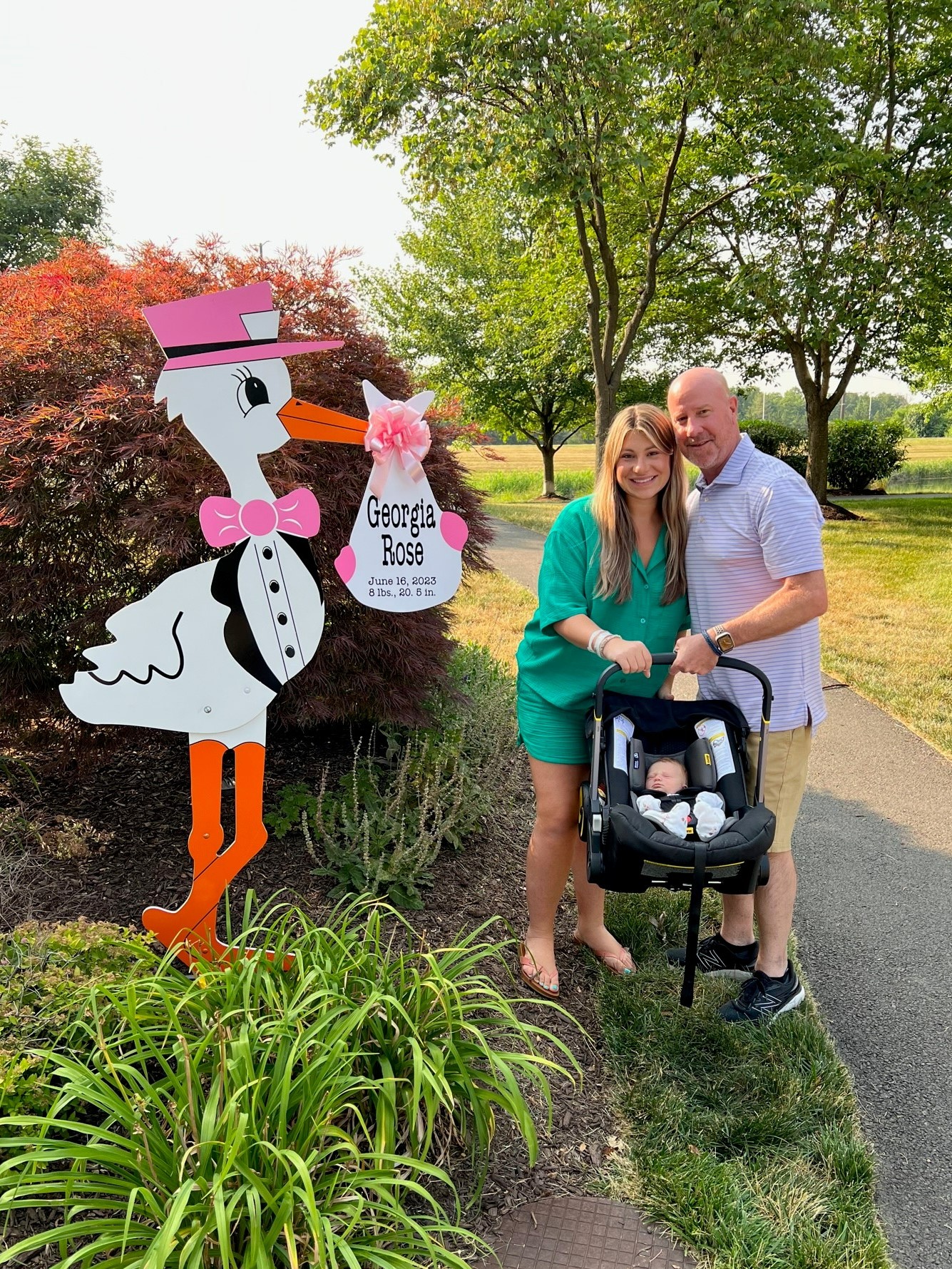 Alan, Abby and Georgia (grandad, new mom and baby), stand in front of a stork sign with Georgia Rose's name on it.