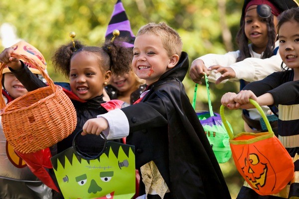 Children dressed up in costumes holding their candy baskets out as they wait to receive candy.