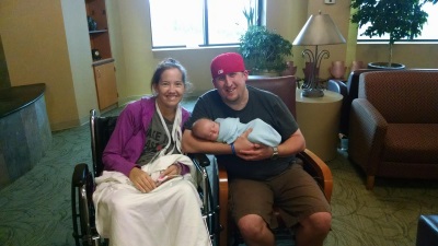Molly and Tom smiling with newborn baby Nolan, in a hospital lounge area.