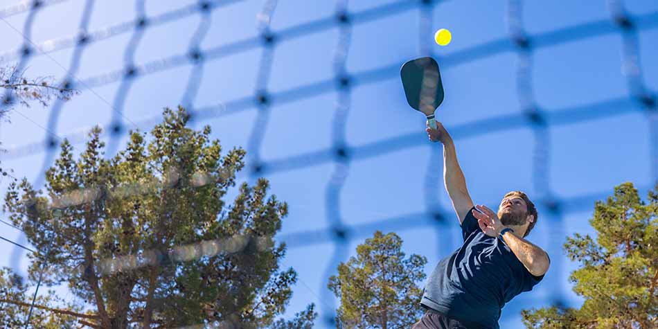 A player hits a yellow pickleball with a blue racket in an overhand spike.