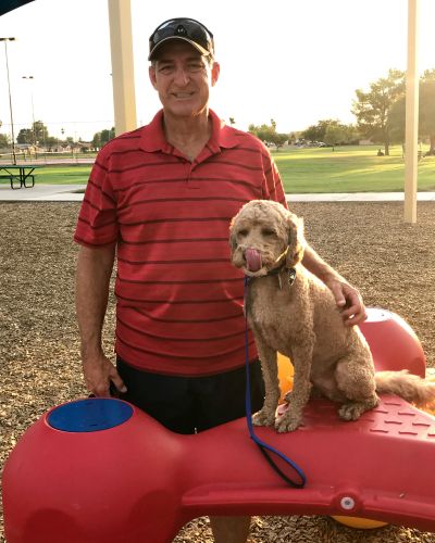 Bud Chew standing next to his caramel colored poodle at a dog park.