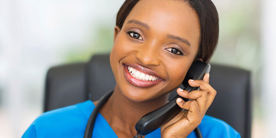 A nurse smiles while holding an office phone up to their face.